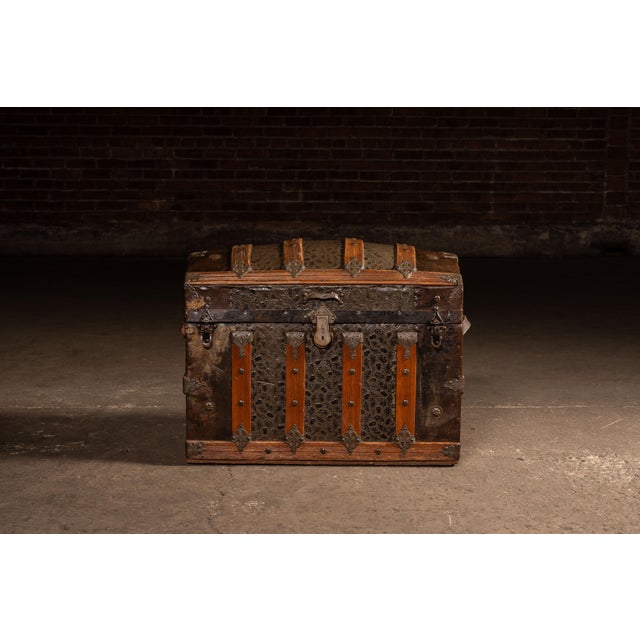 Domed top steamer trunk clad in embossed metal with repeating floral pattern, reinforced by vertical wood slats and...