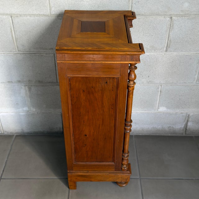 A distinctive and functional wooden bedside cabinet, embellished with turned side columns and a top with a geometric inlay...