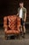 Large Chesterfield wingback chair upholstered in tufted brown vinyl over a hardwood frame. The design combines the deep...