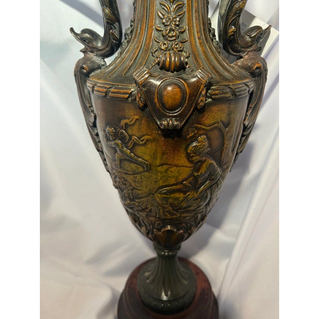 A handsome decorative urn crafted in dark patinated brass and presented on a contrasting wood base. The aged brass finish...