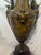 A handsome decorative urn crafted in dark patinated brass and presented on a contrasting wood base. The aged brass finish...