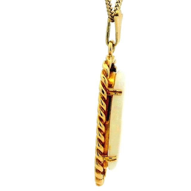 Elegant vintage pendant featuring a luminous oval white opal cabochon set in 18 karat yellow gold, most likely crafted in...