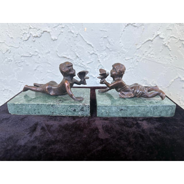 This charming pair of sculptural figures depicts two reclining cherubs, each delicately holding a bird, captured in a...