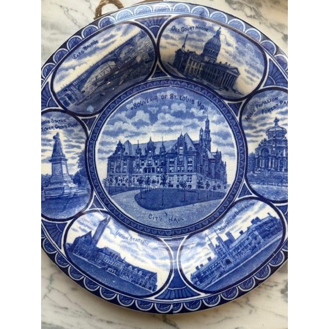 A beautiful antique blue-and-white transferware souvenir plate featuring iconic landmarks of St. Louis, Missouri. Produced...