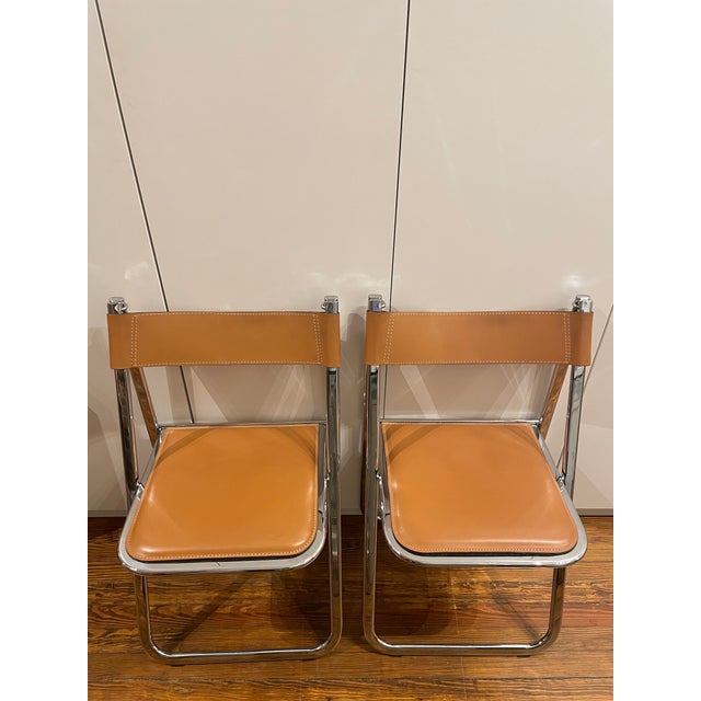 Made in Italy by Arrben, a pair of original "Tamara" Folding Chairs in a Cognac color. Thick saddle leather and polished...