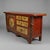 A richly weathered Tibetan cabinet console featuring hand-painted floral and figurative panels in subdued cinnabar red,...