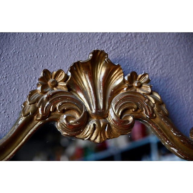 Gilded and lavishly ornamented, this Baroque mirror reflects the somewhat theatrical elegance of the Louis XV style. Its...