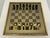 Mid-Century modern chess set with brass and gunmetal pieces on a mirrored glass board. The glass playing board is inset in...