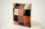 Bold and artisanal, this 16-inch square throw pillow showcases a patchwork checkerboard of orange, black, and cream...