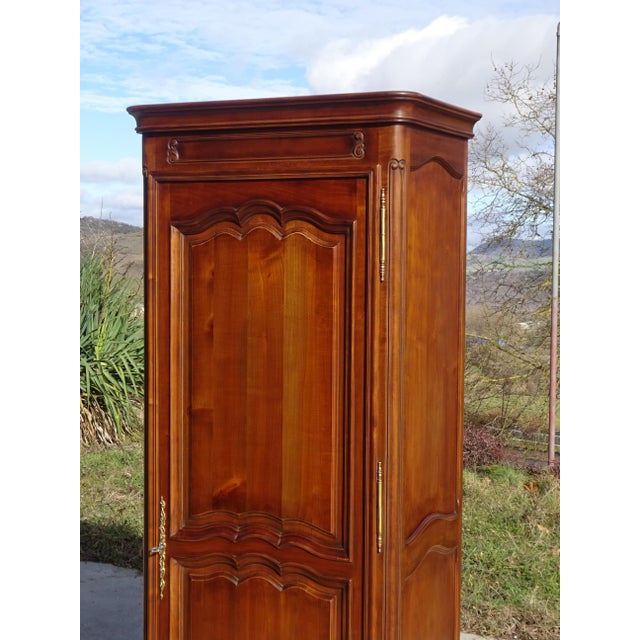 A bonnetière (wardrobe) crafted entirely from solid cherry wood, traditionally made in France in the 1980s. This tall,...