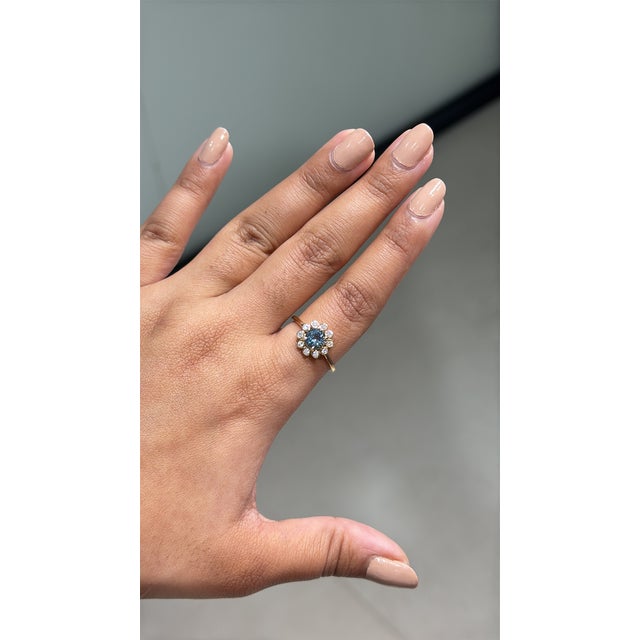 This sunburst halo ring featuring a vibrant 0.71 carat blue topaz and diamonds, set in 14K yellow gold. The center stone...