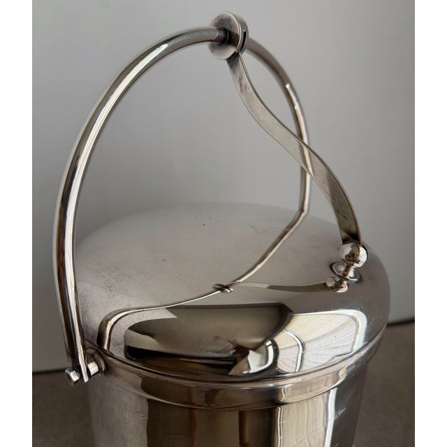 Vintage silver-plate ice bucket with a clean cylindrical form and sculptural swing handle detail. The curved support arm...
