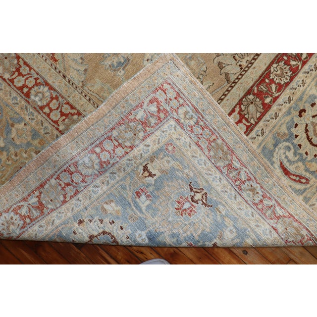 An oversize Persian Meshed rug with an all-over formal design on a khaki field, an icy blue border, accent colors in red...