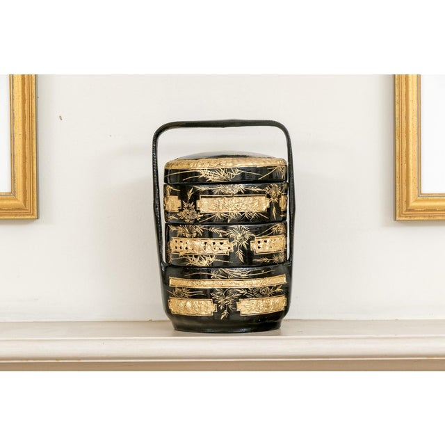 An antique Chinese black lacquered three-tiered wedding basket with a tall arched carrying handle, domed lid, gilt-...
