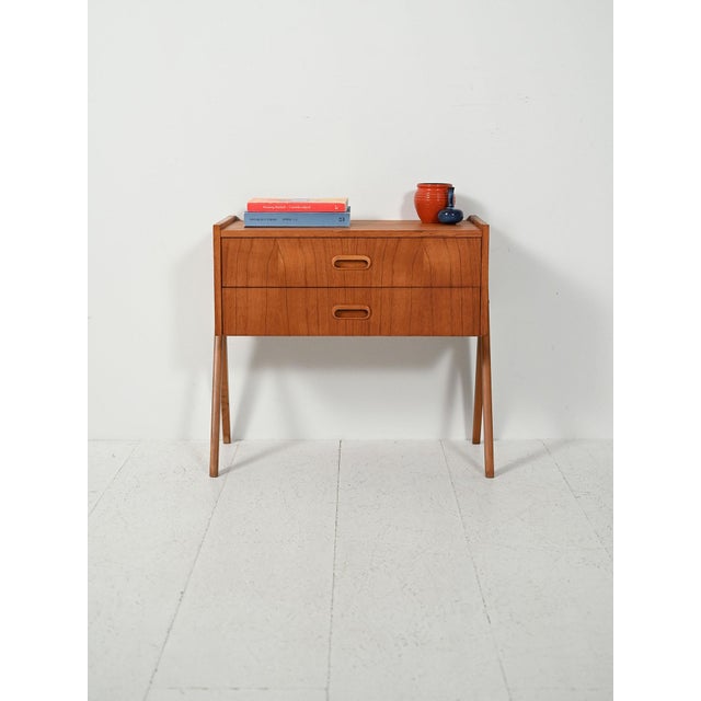 Scandinavian teak bedside table from the 1960s with two drawers, recessed oval handles, and a slender frame on slanted...