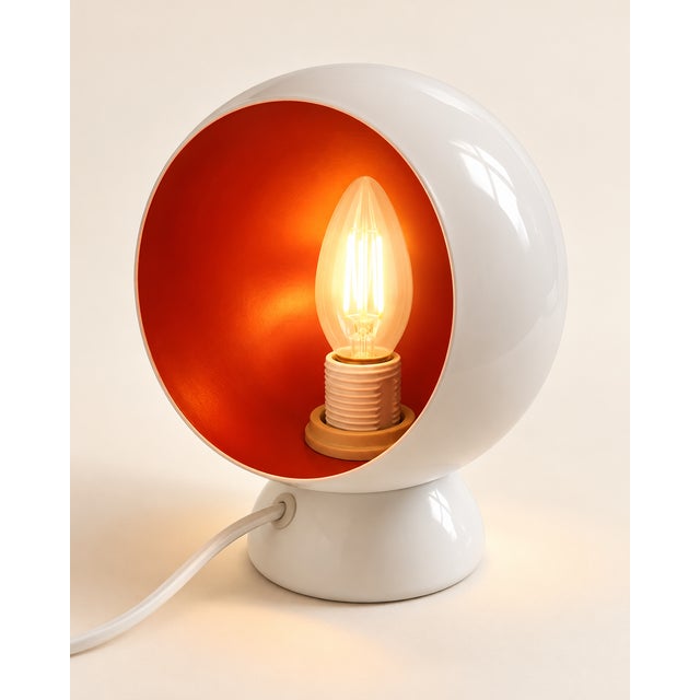 A striking vintage Space Age table lamp with a sculptural rounded form, glossy white exterior and bold red-orange...