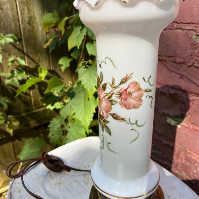 This vintage table lamp features a hand-painted floral design on white glass with a brass base and ruffled edge. It adds...