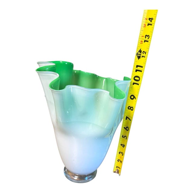 Sculptural art glass vase featuring a vivid green interior, an opaque white exterior, and a dramatically ruffled opening....