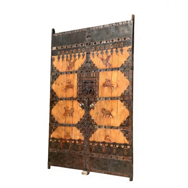 This pair of antique doors showcases a blend of rustic pinewood and hand-forged artwork. Adorned with traditional motifs...