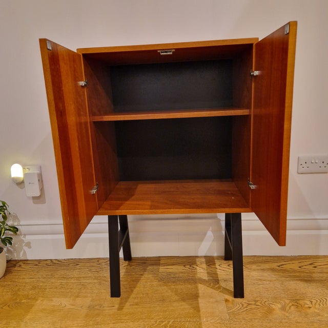 A beautifully crafted mid-century modern teak cabinet featuring sleek black tapered legs and minimalistic design. This...