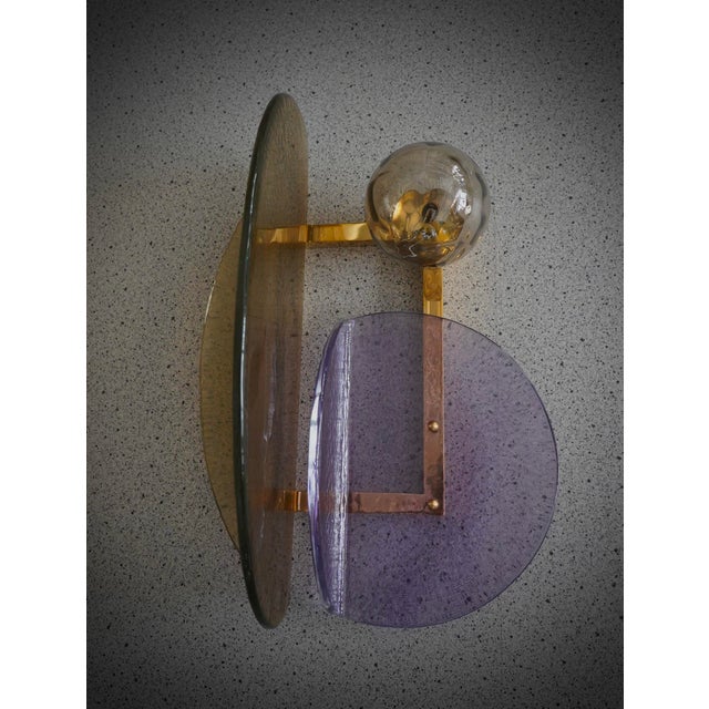 A pair of Murano wall sconces with a distinctive design, featuring a brass frame and distinctive amber and violet glass....