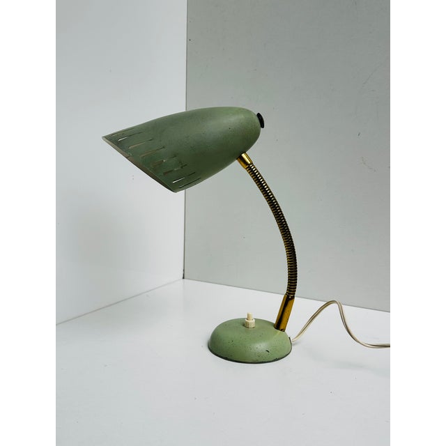 A 1950s table lamp with a slotted metal shade in its original pistachio green. The flexible brass gooseneck and brass...