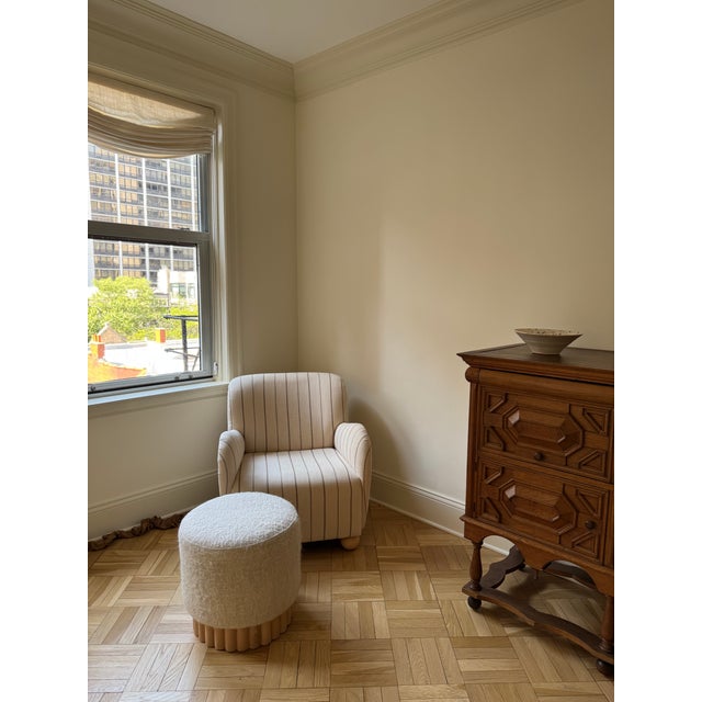 This is a modern round ottoman featuring a minimalist and sculptural design. It has a soft, textured upholstery in a...