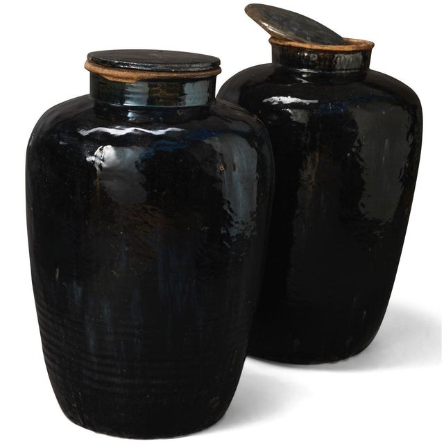 These old stoneware jars each come in a shiny black glaze with a lid and would have been used for storing wine or...
