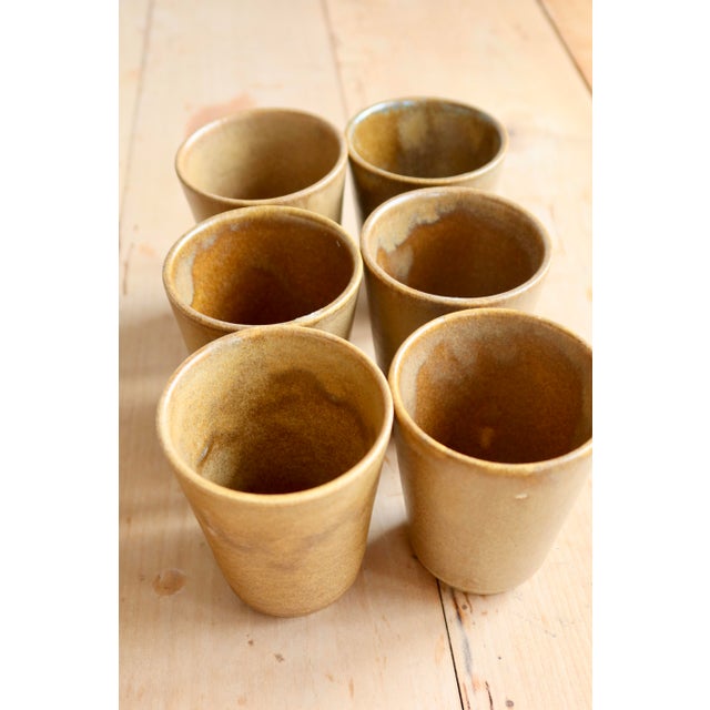 Six stoneware tumblers, from different manufacturers, in warm shades ranging from beige to honey brown. Their slightly...