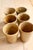 Six stoneware tumblers, from different manufacturers, in warm shades ranging from beige to honey brown. Their slightly...