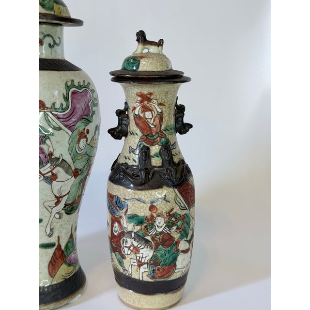 An arresting garniture set of three antique Chinese figural vases, richly decorated with hand-painted warrior and court...