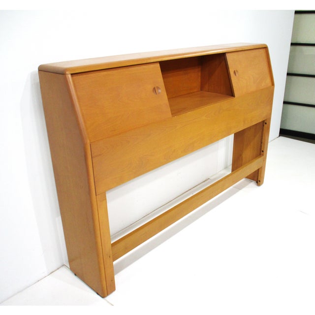 A full-sized headboard with double sliding doors and three storage bins in a champagne finish manufactured by the Heywood...