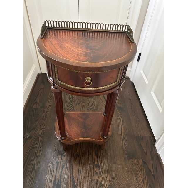 Elegant mahogany veneered demilune bedside or telephone table featuring a finely cast antiqued brass gallery above a...