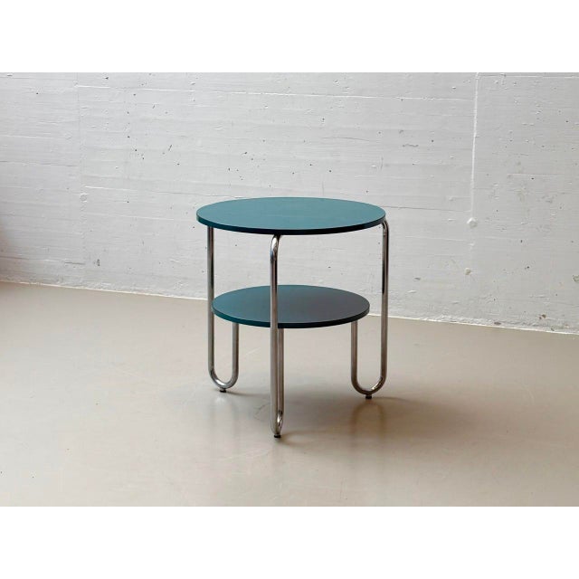 A clearly designed side or coffee table with a round tabletop in petrol-colored Formica laminate on a solid wood base. The...