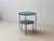 A clearly designed side or coffee table with a round tabletop in petrol-colored Formica laminate on a solid wood base. The...