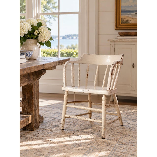 This antique Windsor captain’s chair dates to the early 20th century and features a continuous curved back and arms,...