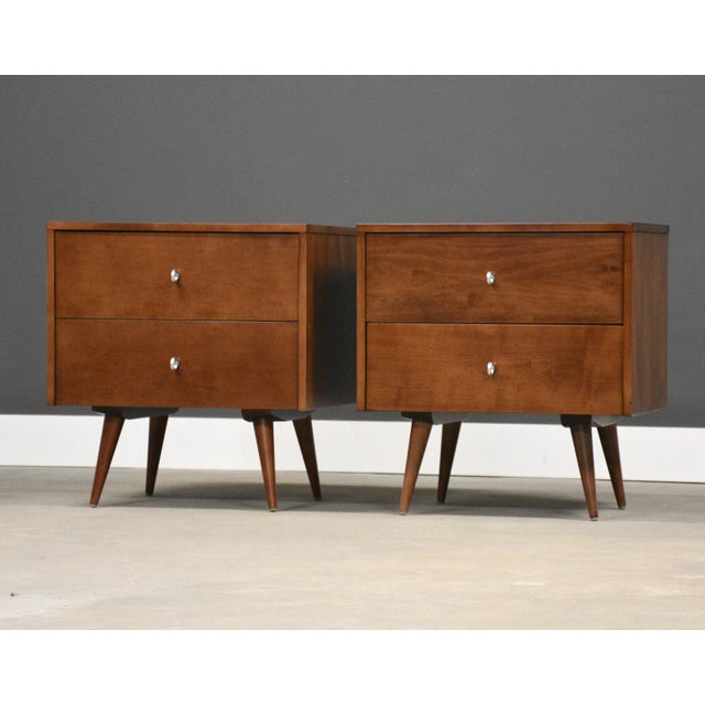 A pair of mid century modern solid maple two drawer nightstands with aluminum ring pulls and canted legs designed by Paul...
