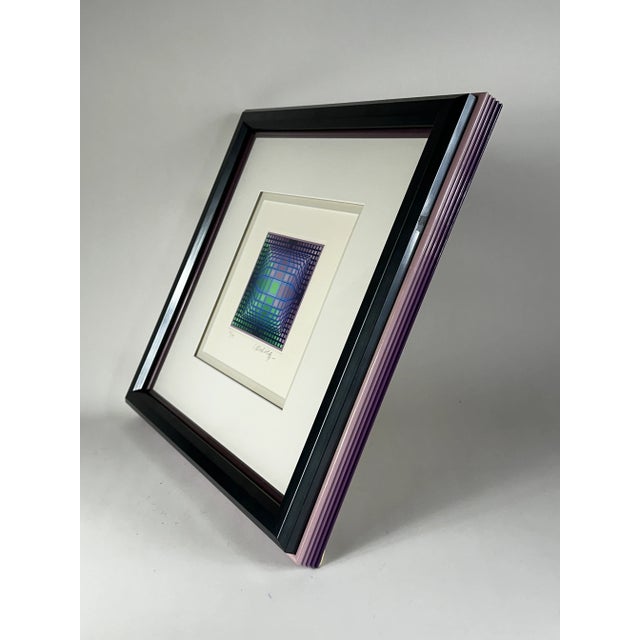Silkscreen lithograph signed and numbered by Victor Vasarely. In hues of purple, green and blue with coordinating frame.