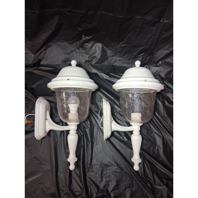 White outdoor wall lantern sconces featuring classic domed caps, clear seeded glass shades, and brass hardware. These each...