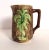 This antique English Majolica pottery pitcher has a textured brown bark body superimposed by a green palmetto/cabbage palm...