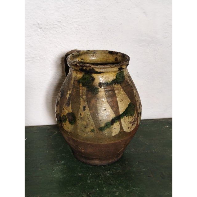 Rustic terracotta jug, handcrafted in Southern Italy, with a rounded body, a wide handle, and a thick, slightly flared...