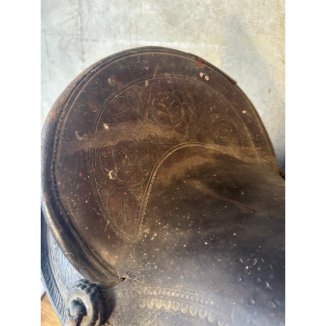 This is a vintage Western saddle featuring classic floral tooling on the leather. It has a well-worn, rustic patina that...