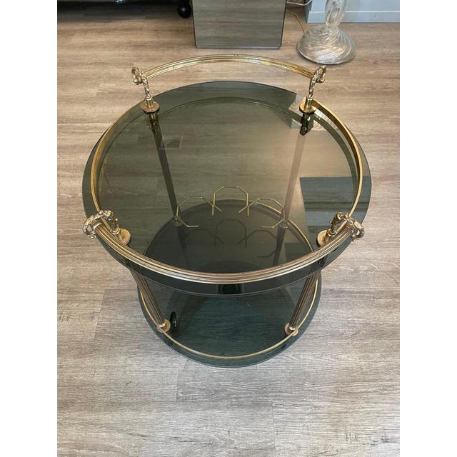 A 1970s trolley with a brass frame and smoked glass shelves. There are four brass legs, each with a wheel at the bottom, a...