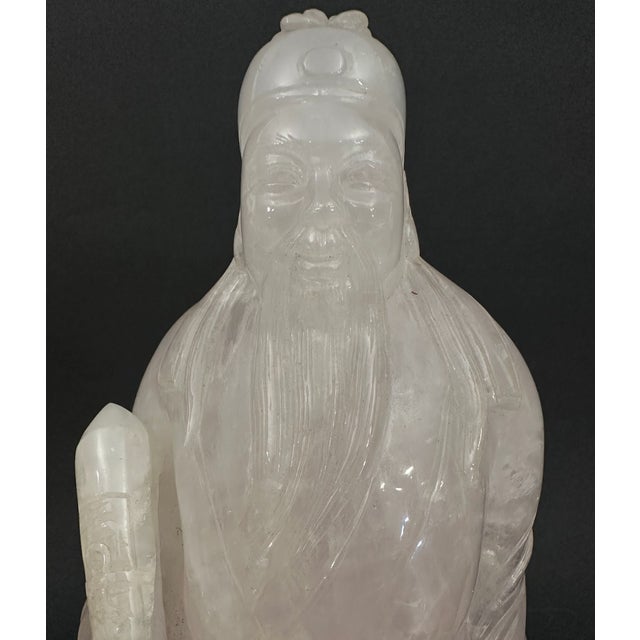 A Taoist priest carved of crystal, he is pictured here enrobed with a scroll in his hand and an headdress on his head. In...