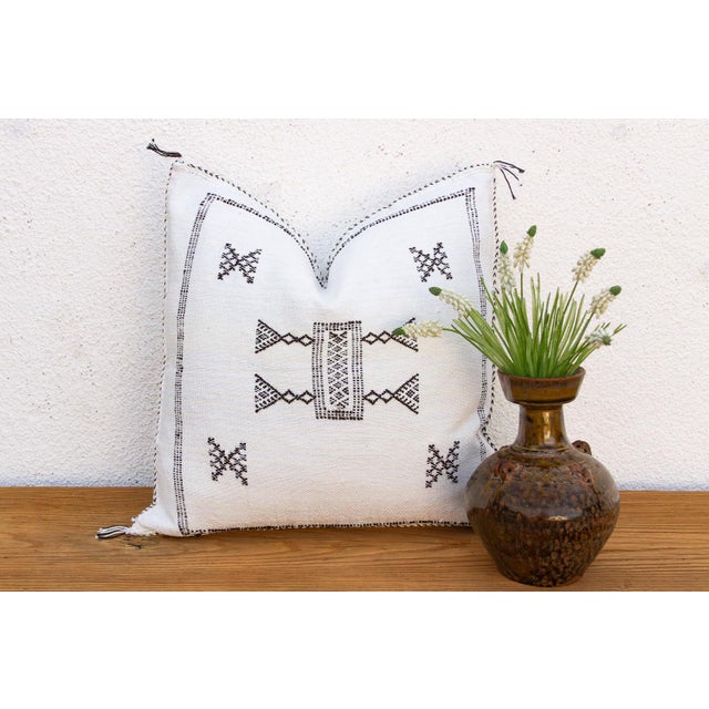 A bowtie medallion anchors the center of this handcrafted Moroccan cactus silk pillow, echoed by crossed-X motifs at each...