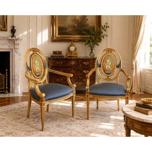 A charming pair of Louis XVI style armchairs featuring hand-painted oval medallion backs framed within elegant giltwood-...