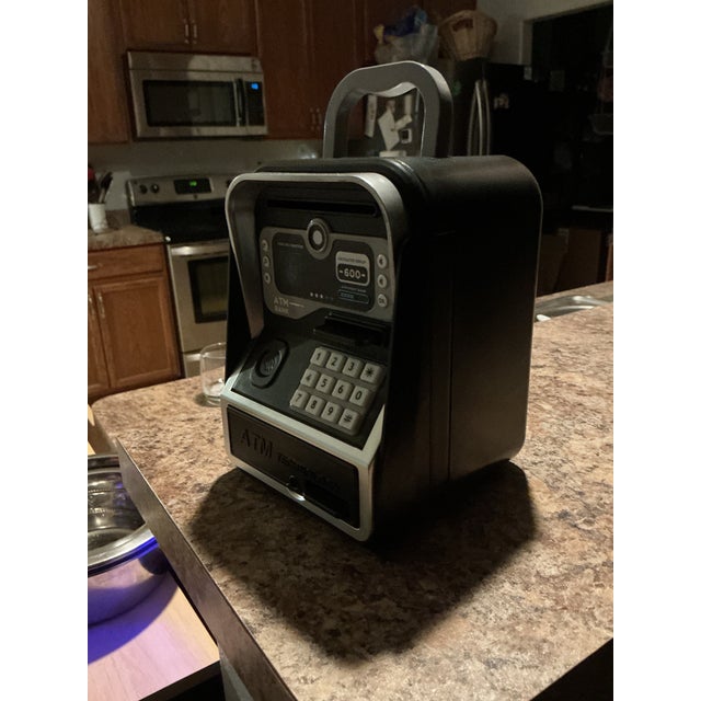 Electronic ATM-style savings bank for kids in black and silver. Designed like a miniature ATM, this interactive money bank...