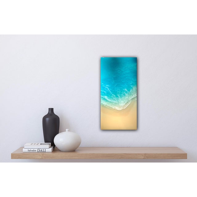 This artwork depicts a serene coastal scene, capturing the gentle transition of turquoise waters meeting a soft, sandy...