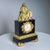 A mantel clock with a black case and gilt bronze appliqués. The dial with Roman hours. with a figural finial in the shape...