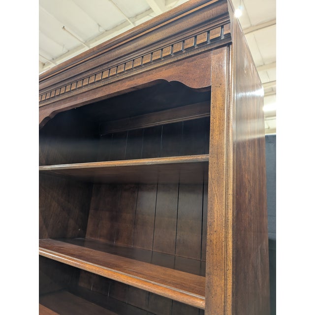 This tall, dark-stained wooden cabinet features classic styling with an ornate crown molding detail. The upper section...
